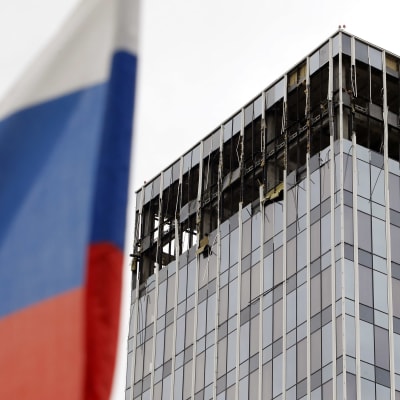 Ett höghus med utblåsta fönster. I förgrunden syns Rysslands flagga.
