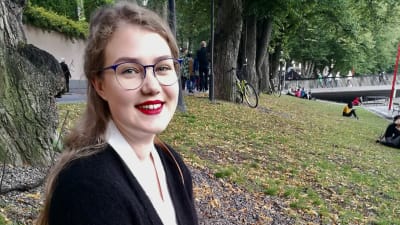 Kvinna med långt, ljust hår sitter på gräsmatta. 