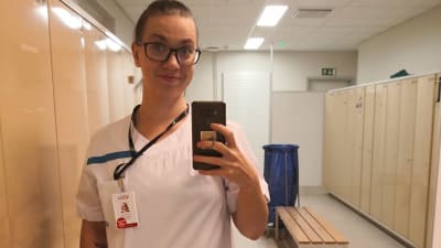 En kvinna i sköterskeuniform tar en selfie i ett omklädningsrum.