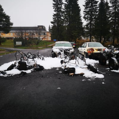 Kuvassa palaneita ja vaurioituneita autoja Keminmaan kirjaston parkkipaikalla.