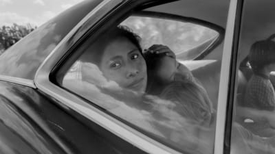 Cleo (Yalitza Aparicio) sitter i baksätet i en bil och ser ut genom fönstret.