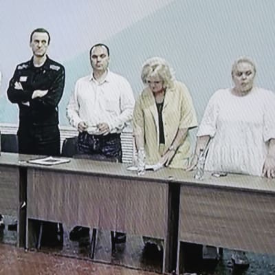 Bild fotograferad från en TV-skärm. Navalnyj står med några andra personer i ett rått rum. Navalnyj har armarna i kors.