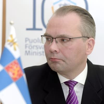 Porträtt på försvarsminister Jussi Niinistö vid en standard med finska flaggan.