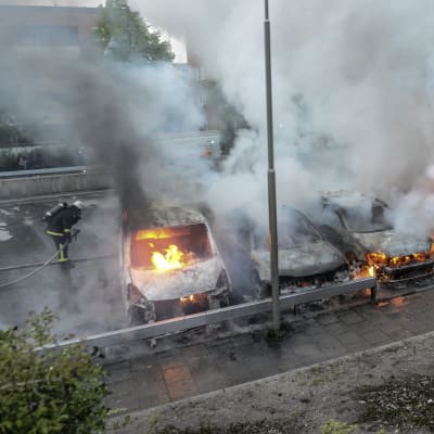 Fyra bilar står i lågor på en gata.