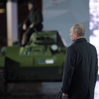 Vladimir Putin seisoo. Taustalla panssarivaunu.