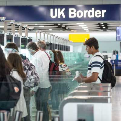 Människor använder passkontrollautomater på ett brittiskt flygfält. Ovanför människorna som står i den långa raden automater finns en skylt med texten "UK Border" (Storbritanniens gräns).