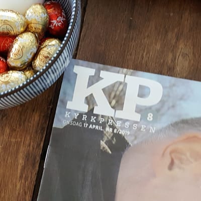 Kyrkpressen tidningen ligger på ett bord vid en skål med påskägg