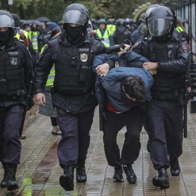 Tre poliser med hjälmar och en gripen demonstrant i centrum av Moskva.