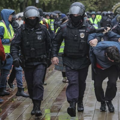 Tre poliser med hjälmar och en gripen demonstrant i centrum av Moskva.
