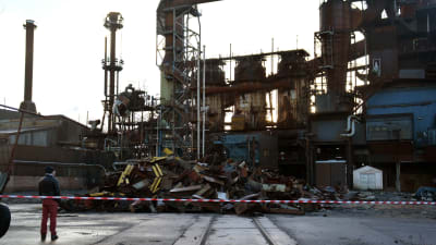 En person står och tittar på en hög med bråte framför en gammal stålfabrik.