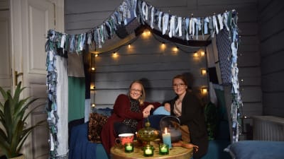 Två kvinnor som sitter i en soffa med en tyghimmel.