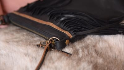 Detaljer av en svart läderhandväska med fransar.