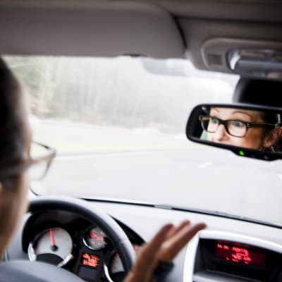En kvinna slår ut med händerna vid ratten i en bil. Hon ser ilsken ut i backspegeln.