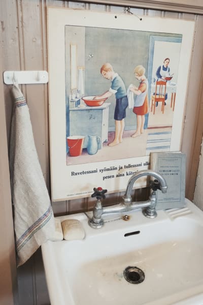 Gammalt tvättställ, ovanför det en skolaffisch med anvisningar om hur man korrekt tvättar sina händer.