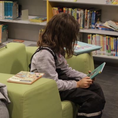 Två stycken barn sitter och läser i ett bibliotek.