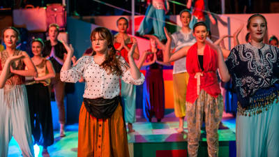 Ungdomar dansar en bollywoodinspirerad dans i ungdomsshow i Pargas. I förgrunden Saga Rosenlund i vit skjorta med svarta prickar.