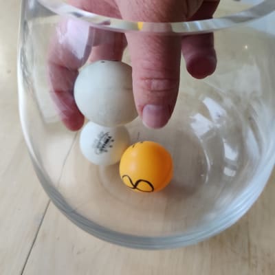 Tre pingisbollar i en glasburk, en hand lyfter upp en av bollarna.