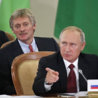 Putins talesman Dmitrij Pdeskov strax bakom president Putin under en konferens i Sotji den 11 oktober 2017.