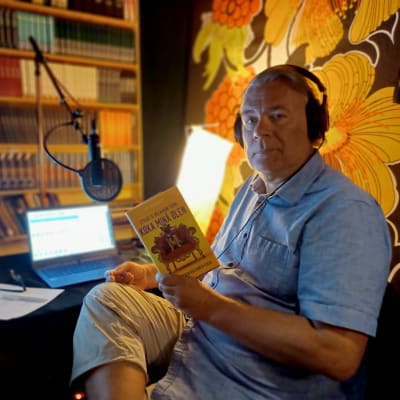 Ari Turunen äänikirjoja lukemassa, studiossa joka on sisutettu kirjoin ja kirjahyllyin.