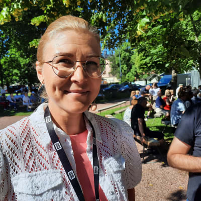 SDP:n kansanedustaja Niina Malm seisoo ulkona auringonpaisteessa, taustalla näkyy puita ja ihmisiä.