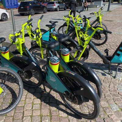 Rykelmässä polkupyöriä, joissa kaikissa neon-keltaiset sarvet, musta satula ja logolla varustettu turkoosi mainospaneeli. 