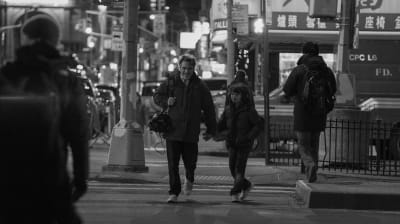 En medelålders man och en liten pojke promenerar hand i hand över ett övergångsställe i en storstad.