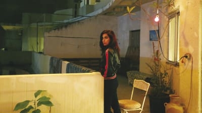 Yasmine Hamdan på en balkong på kvällen. en växt i kruka.