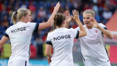 Vitklädda norska damfotbollspelare gör high-five.