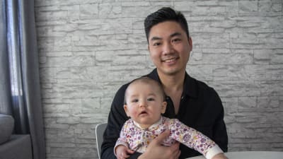 En man från Vietnam sitter vid ett bord med ett litet barn i famnen.