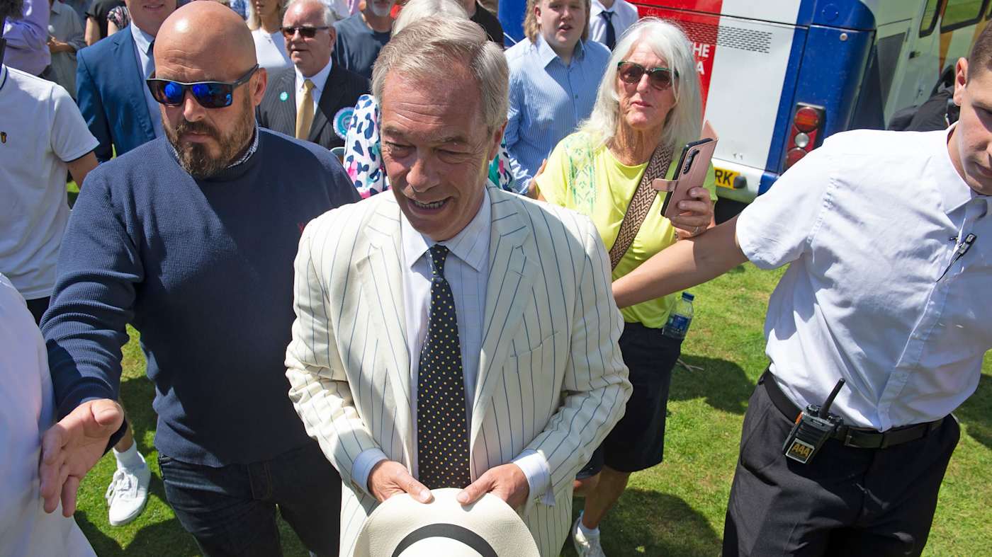 Nigel Farage in a striped suit surrounded by people during a campaign rally.
