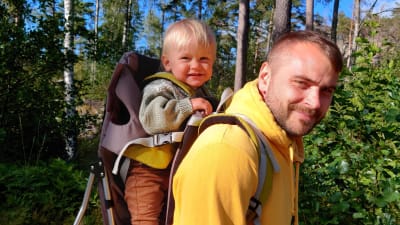 Johannes Björkqvist bär sitt barn i en ryggsäck på ryggen. De är ute på skogspromenad.