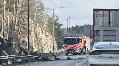 En hög stora stenar har rasat in på en bilväg. I bakgrunden syns en brandbil.