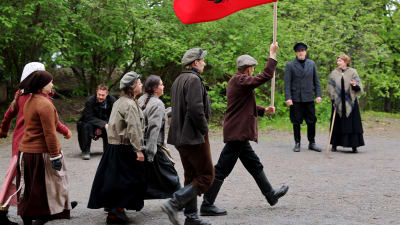 Rooliasuihi pukeutuneita ihmisiä marssimassa punaisen lipun kanssa Pyynikin kesäteatterin harjoituksissa.