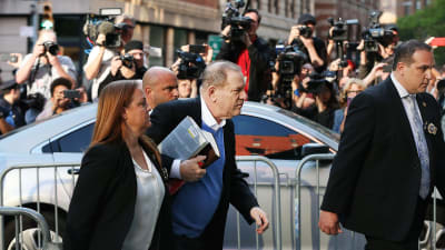 harvey Weinstein med en hög böcker under armen och pressen i bakgrunden överlämnar sig till polisen i New York.