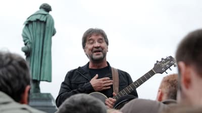 Jurij Sjevtjuk med en gitarr. I förgrunden publikens huvuden och i bakgrunden en staty.