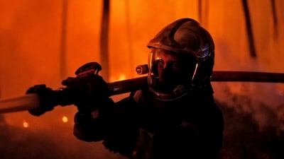 Brandman sprutar vatten mot en skogsbrand i Gironde i Frankrike medan elden härjar skogen i bakgrunden.