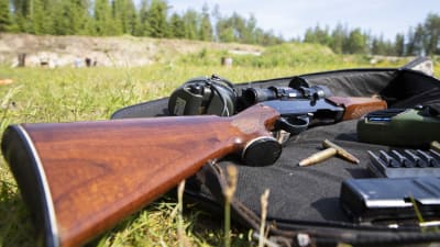 Kiikaritähtäimellä varustettu kivääri, patruunoita ja kuulosuojaimet aseenkantolaukun päällä Kiuruveden ampumaradalla.