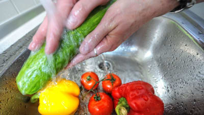 En närbild av händer som tvättar grönsaker under vattenkran.
