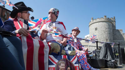 tre män i kläder prydda med storbritanniens färger blått, rött och vitt sitter framför Windsor slott