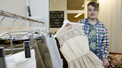 Anton West håller upp en vit klänning som han designat och sytt av gamla tyger.