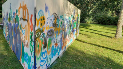 En triangelformad vägg eller ett plank som placerats ute på en gräsmatta. Det är gatukonst, graffiti målat på väggen.
