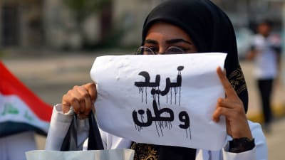 en kvinnlig demonstrant håller upp en lapp med "Vi behöver ett land".