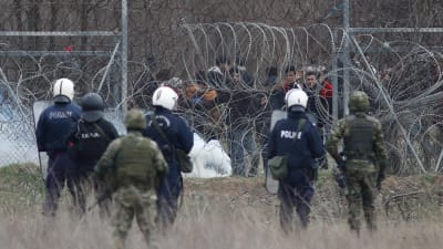 Grekiska poliser och militärer betraktar migranter på den turkiska sidan av gränsen mellan Grekland och Turkiet i Kastanies/Pazarkule.