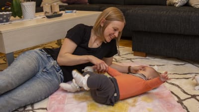 En kvinna ligger på sitt vardagsrumsgolv och leker med sin bebis.