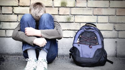 En ensam pojke sitter lutad mot en vägg med huvudet mot knäna.