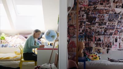 På bilden syns klimataktivisten Greta Thunberg hemma där hon sitter vid skrivbordet i sitt rum. På skrivbordet står en jordglob och en vägg är helt fylld av affisher och foton.