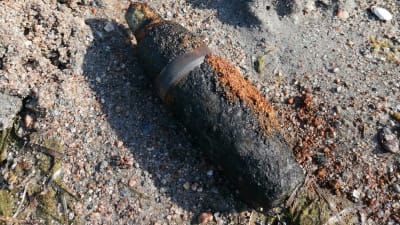 En granat i närbild på en sandstrand plus ett blått öskar av plast.