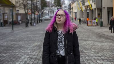 En kvinna med rosa hår och svart jacka. Går på en gågata i Jakobstad. 