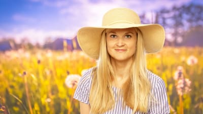Karin Storbacka står på en sommaräng med en stor solhatt på huvudet.
