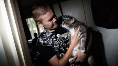 Ung man håller en grå katt i famnen.